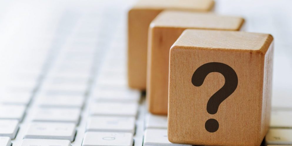 Small wooden dices with question mark on one side, sitting on computer keyboard and viewed in close-up with blurred copy space